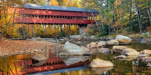 Classic timber covered bridge crossing a rural river corridor in autumn